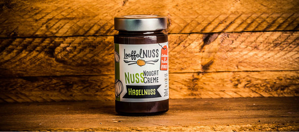 Ein Glas Loeffelnuss Nuss-Nougat-Creme Haselnuss vor Holzhintergrund